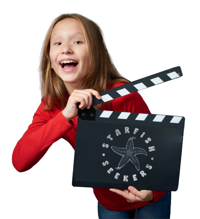 Happy pre-teen girl in a long sleeve red shirt with a clapperboard ready to shut, and the Starfish Seekers logo on the face of the board.